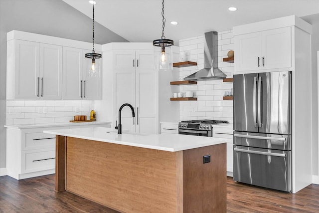 kitchen featuring decorative light fixtures, a center island with sink, wall chimney range hood, white cabinetry, and appliances with stainless steel finishes