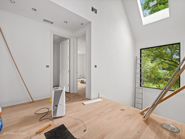 interior space with high vaulted ceiling, a skylight, and light hardwood / wood-style flooring