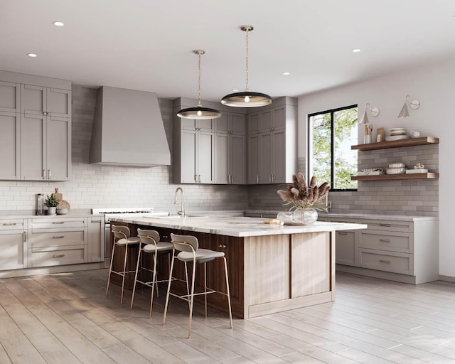 kitchen with tasteful backsplash, a kitchen bar, a kitchen island with sink, gray cabinets, and premium range hood