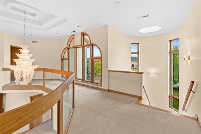 hall featuring a healthy amount of sunlight, light carpet, and a chandelier