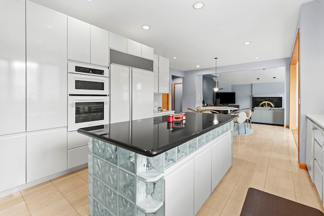 kitchen with white cabinetry, paneled built in fridge, a kitchen island, hanging light fixtures, and double oven