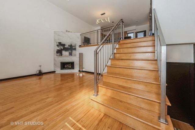 stairs featuring wood-type flooring, lofted ceiling, and a high end fireplace