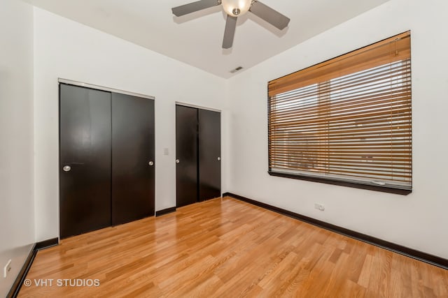 unfurnished bedroom with light wood-type flooring, ceiling fan, and multiple closets