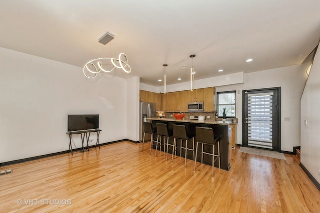 kitchen featuring a breakfast bar area, stainless steel appliances, hanging light fixtures, and light hardwood / wood-style flooring