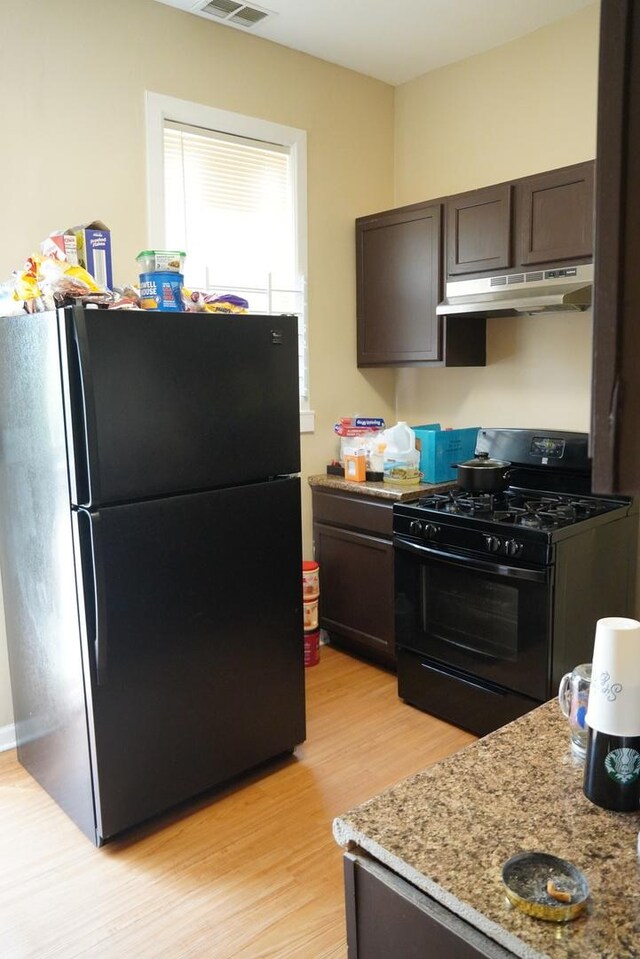 kitchen with dark brown cabinetry, light stone countertops, black appliances, and light hardwood / wood-style floors