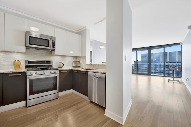 kitchen featuring expansive windows, stainless steel appliances, light hardwood / wood-style floors, light stone counters, and white cabinetry