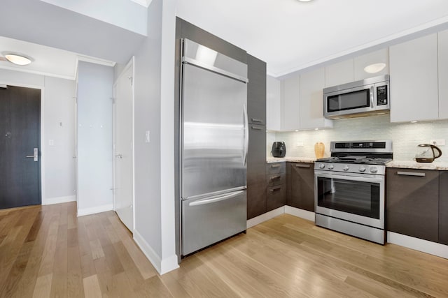 kitchen with white cabinets, light stone countertops, backsplash, appliances with stainless steel finishes, and light hardwood / wood-style floors