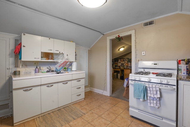 kitchen featuring white cabinetry, white gas stove, sink, light tile floors, and vaulted ceiling