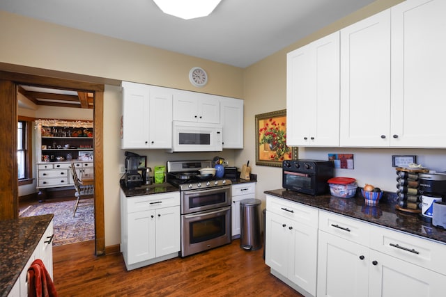 kitchen with range with two ovens, dark stone counters, white cabinets, and dark hardwood / wood-style floors