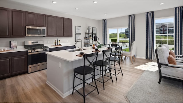 kitchen featuring light hardwood / wood-style flooring, stainless steel appliances, sink, a center island with sink, and a breakfast bar area