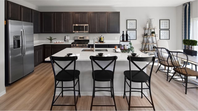 kitchen with dark brown cabinets, a kitchen bar, appliances with stainless steel finishes, light hardwood / wood-style floors, and sink