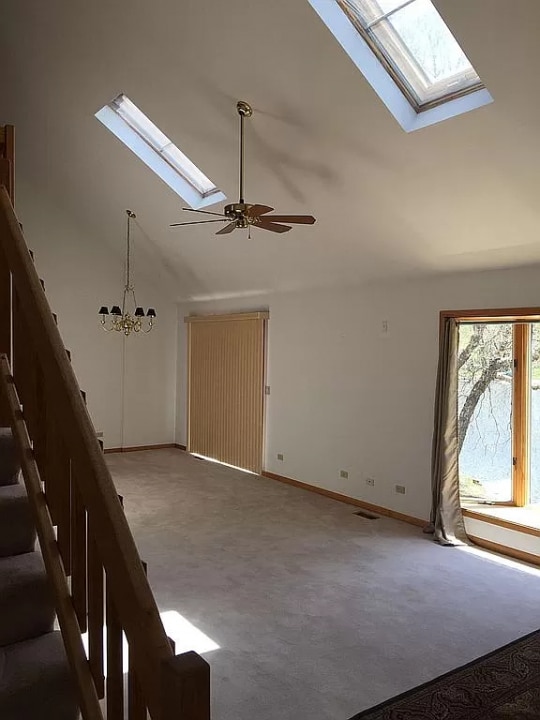 unfurnished living room featuring carpet flooring, a skylight, high vaulted ceiling, and ceiling fan with notable chandelier