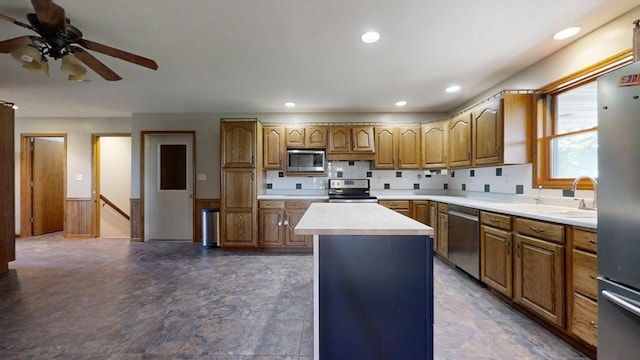 kitchen featuring brown cabinetry, appliances with stainless steel finishes, a center island, light countertops, and a sink