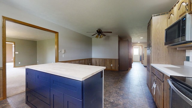 kitchen featuring a wainscoted wall, light countertops, stainless steel microwave, a kitchen island, and ceiling fan