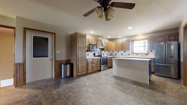 kitchen featuring a wainscoted wall, appliances with stainless steel finishes, brown cabinets, a center island, and light countertops