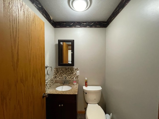 half bath featuring tasteful backsplash, vanity, toilet, and a textured ceiling