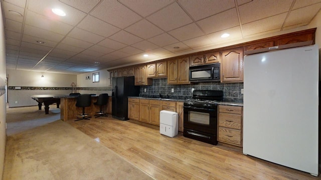 kitchen featuring brown cabinets, dark countertops, decorative backsplash, light wood-type flooring, and black appliances