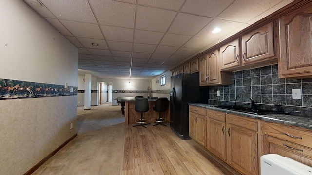 kitchen featuring brown cabinetry, freestanding refrigerator, dark stone counters, and a sink