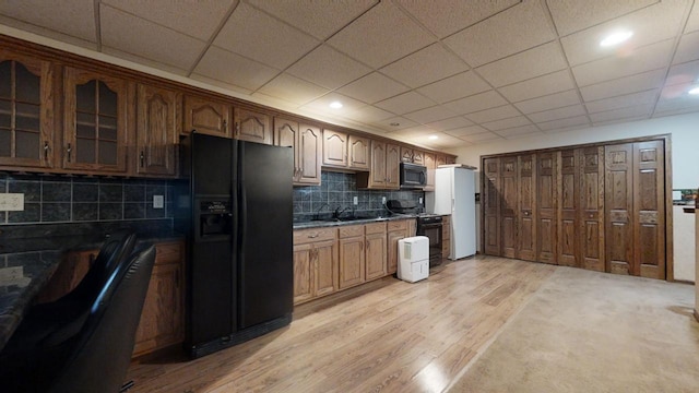 kitchen featuring a paneled ceiling, glass insert cabinets, light wood-type flooring, black appliances, and backsplash