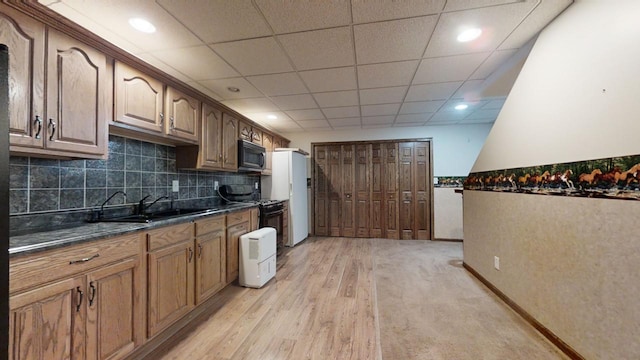 kitchen featuring tasteful backsplash, brown cabinetry, light wood-style flooring, black appliances, and a sink