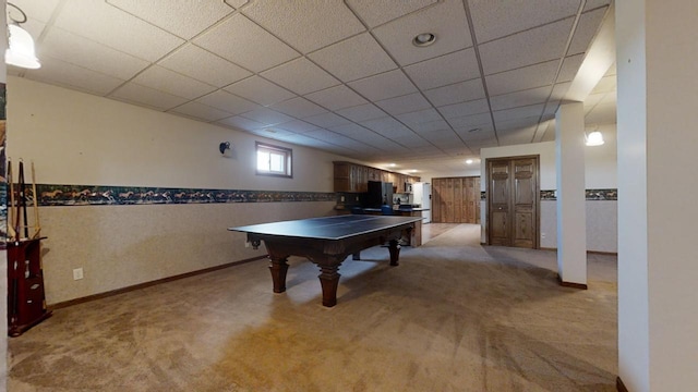 recreation room featuring baseboards, a drop ceiling, and light colored carpet