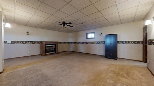 unfurnished living room with a glass covered fireplace, light colored carpet, a wainscoted wall, ceiling fan, and a paneled ceiling