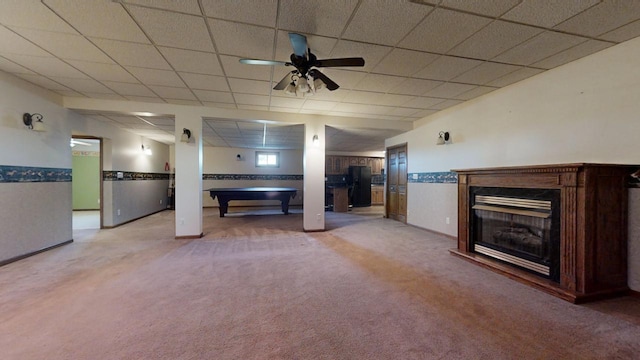 unfurnished living room featuring ceiling fan, a paneled ceiling, a fireplace, baseboards, and carpet