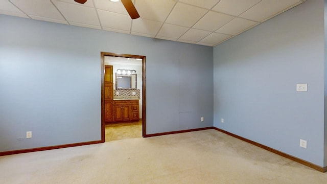 spare room with a ceiling fan, light carpet, a drop ceiling, and baseboards