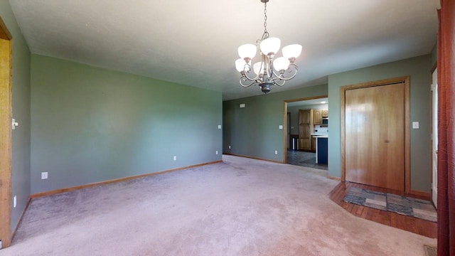 spare room with a chandelier, carpet flooring, and baseboards