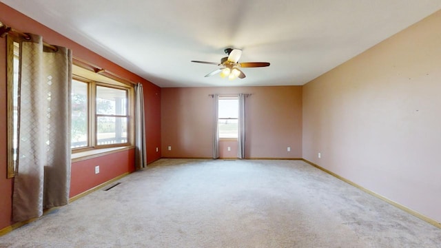 empty room featuring a ceiling fan, light colored carpet, visible vents, and baseboards