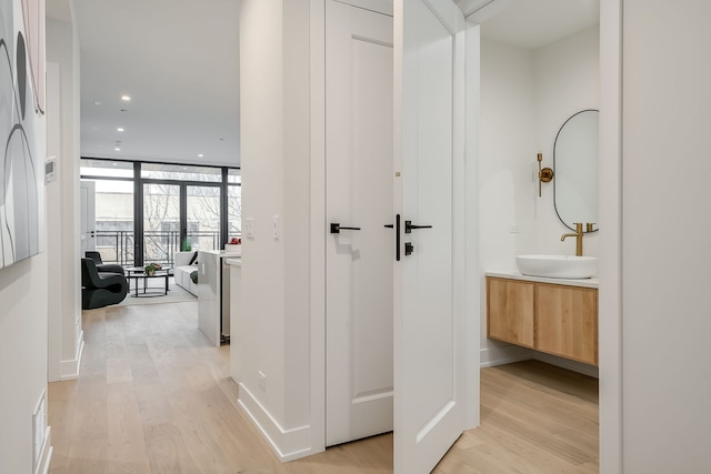 hall featuring floor to ceiling windows, sink, and light hardwood / wood-style flooring