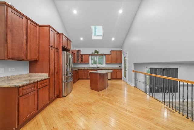 kitchen with light wood-type flooring, a center island, stainless steel fridge with ice dispenser, high vaulted ceiling, and a skylight