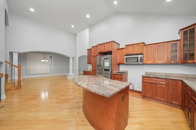 kitchen with light wood-type flooring, light stone counters, a center island, high vaulted ceiling, and appliances with stainless steel finishes