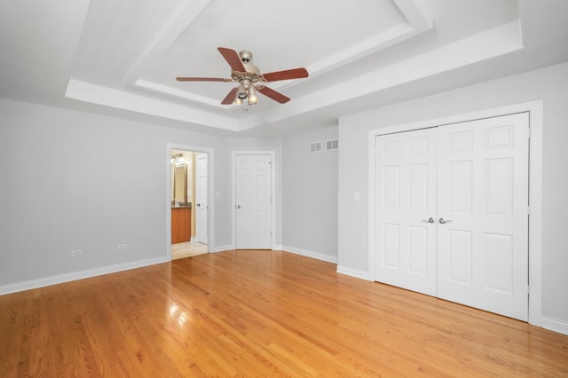 unfurnished bedroom with light hardwood / wood-style floors, a tray ceiling, and ceiling fan