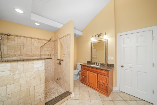 bathroom featuring tile patterned flooring, lofted ceiling, tiled shower, vanity, and toilet