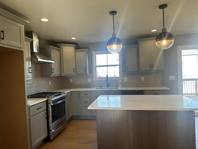 kitchen featuring gray cabinetry, sink, stainless steel gas range, wall chimney exhaust hood, and decorative light fixtures