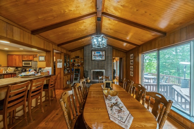 dining room featuring wood walls, a brick fireplace, brick wall, vaulted ceiling with beams, and hardwood / wood-style flooring