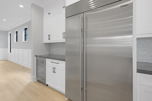 kitchen with stainless steel built in refrigerator, white cabinets, beverage cooler, backsplash, and light hardwood / wood-style floors