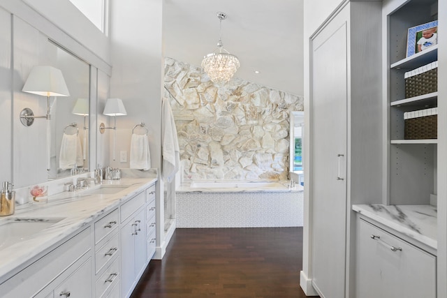 bathroom with a bathtub, double vanity, a chandelier, and wood-type flooring