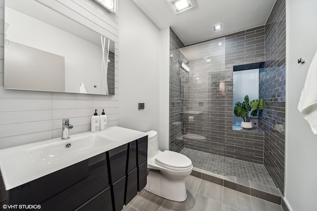 bathroom with tile patterned flooring, toilet, vanity, tile walls, and a tile shower