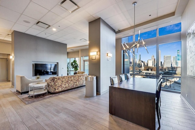 interior space with light hardwood / wood-style flooring, a center island, hanging light fixtures, a paneled ceiling, and dark brown cabinetry