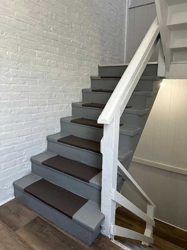 stairs featuring brick wall and dark wood-type flooring