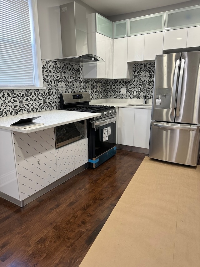 kitchen with wall chimney exhaust hood, white cabinets, dark hardwood / wood-style floors, stainless steel appliances, and tasteful backsplash