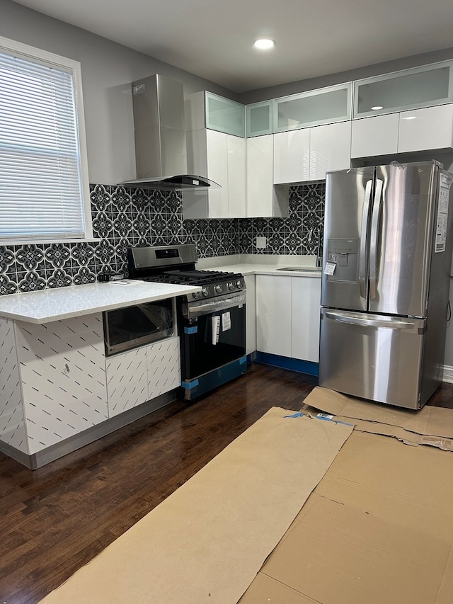 kitchen featuring appliances with stainless steel finishes, backsplash, dark wood-type flooring, wall chimney range hood, and white cabinetry