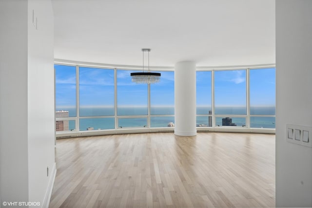 empty room featuring a chandelier, a water view, floor to ceiling windows, and light hardwood / wood-style floors