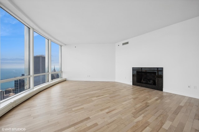 unfurnished living room with plenty of natural light, a water view, light wood-type flooring, and baseboard heating