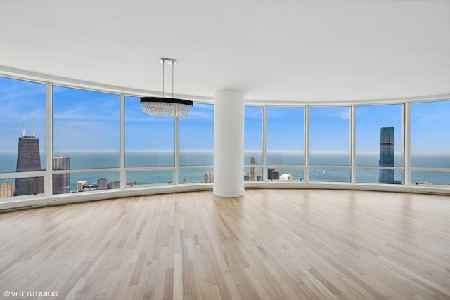 unfurnished living room featuring floor to ceiling windows, a water view, light wood-type flooring, and a chandelier