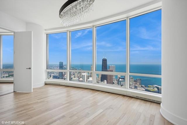 spare room featuring a healthy amount of sunlight, a water view, wood-type flooring, and an inviting chandelier