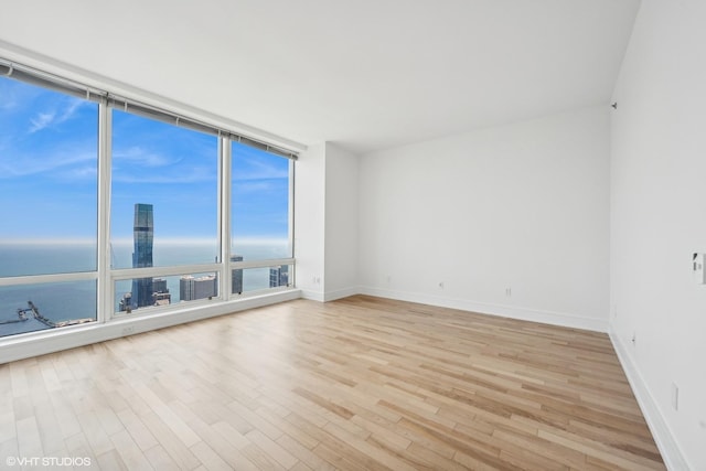 spare room featuring light wood-type flooring, a water view, and expansive windows