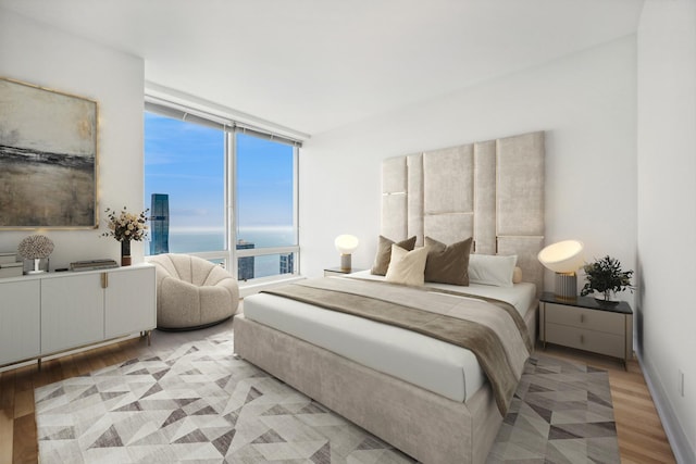 bedroom with a water view, light hardwood / wood-style flooring, and a wall of windows